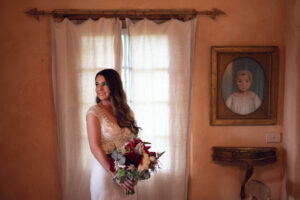 A beautiful bride holding a bouquet, standing in front of a rustic wall