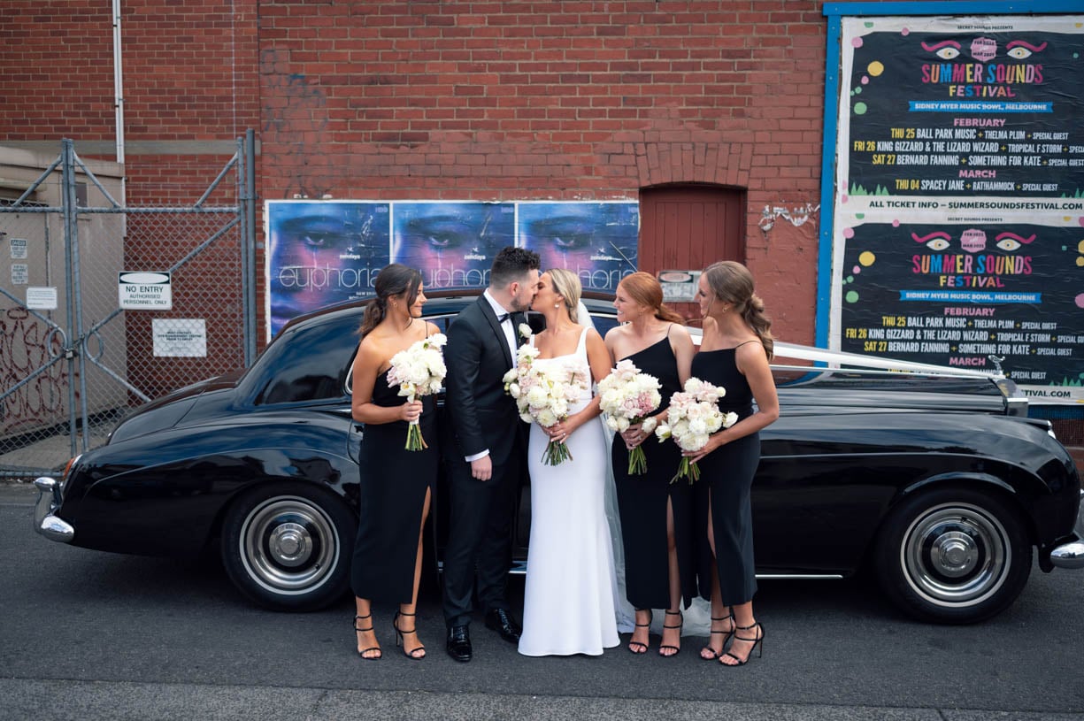 The bridesmaids are watching the couple kiss in front of a luxury car - brisbane wedding photographer 