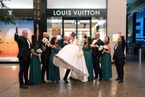 The newlyweds and bridal party cheering in front of the LV store, with the groom lifting the bride for a kiss